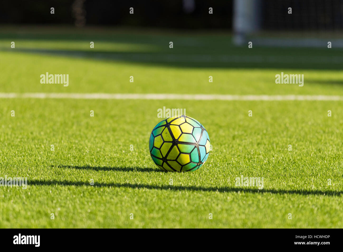 A multicoloured soccer ball on an astro turf soccer field in afternoon sun Stock Photo