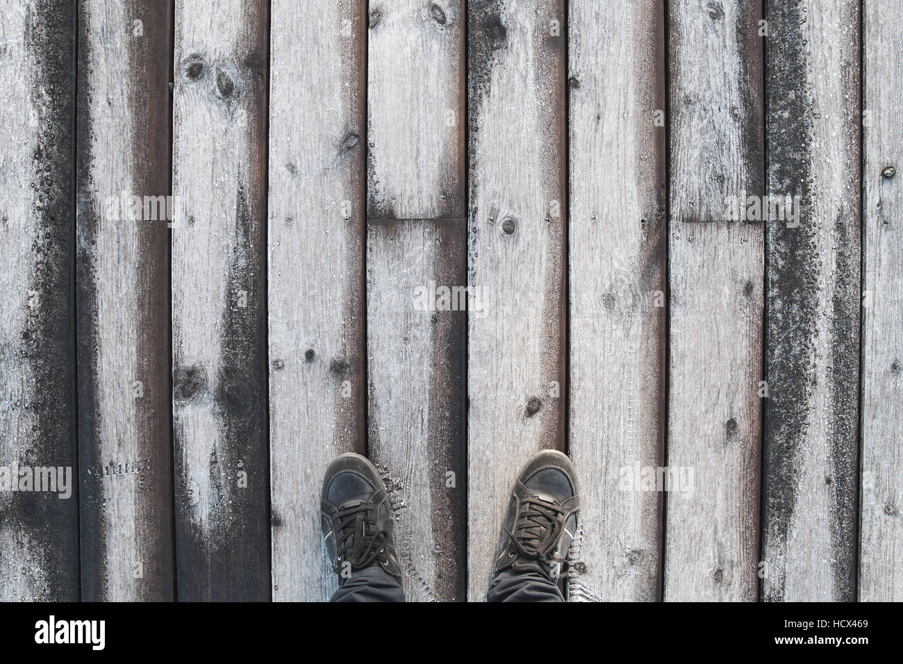 Male feet in black leather shoes stand on old wooden pier floor with frost Stock Photo