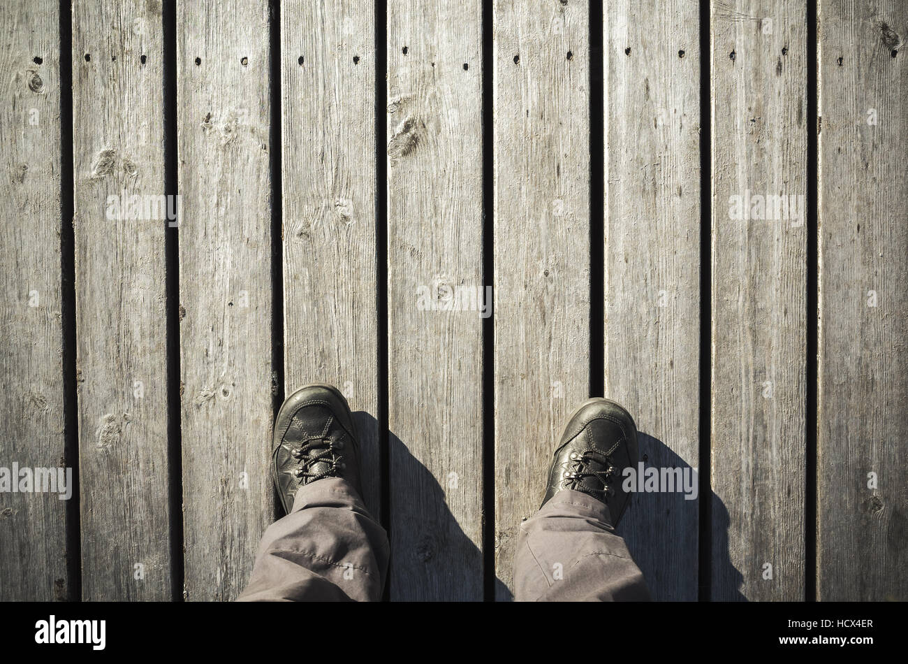 Male feet in black leather shoes stand on old wooden pier floor, first person view. Vintage tonal correction photo filter, old style effect Stock Photo