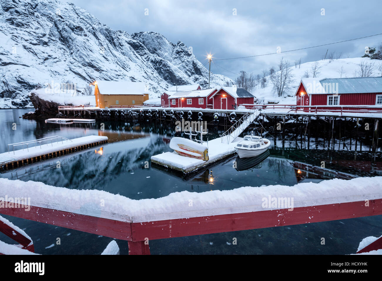 Cold sea and snowy peaks frame the fishing village at dusk, Nusfjord, Nordland, Lofoten Islands, Northern Norway Stock Photo