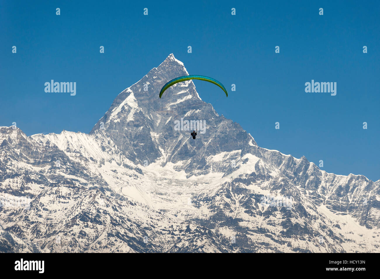 A paraglider hangs in the air with the dramatic peak of Machapuchare (Fishtail mountain) in the distance, Nepal Stock Photo