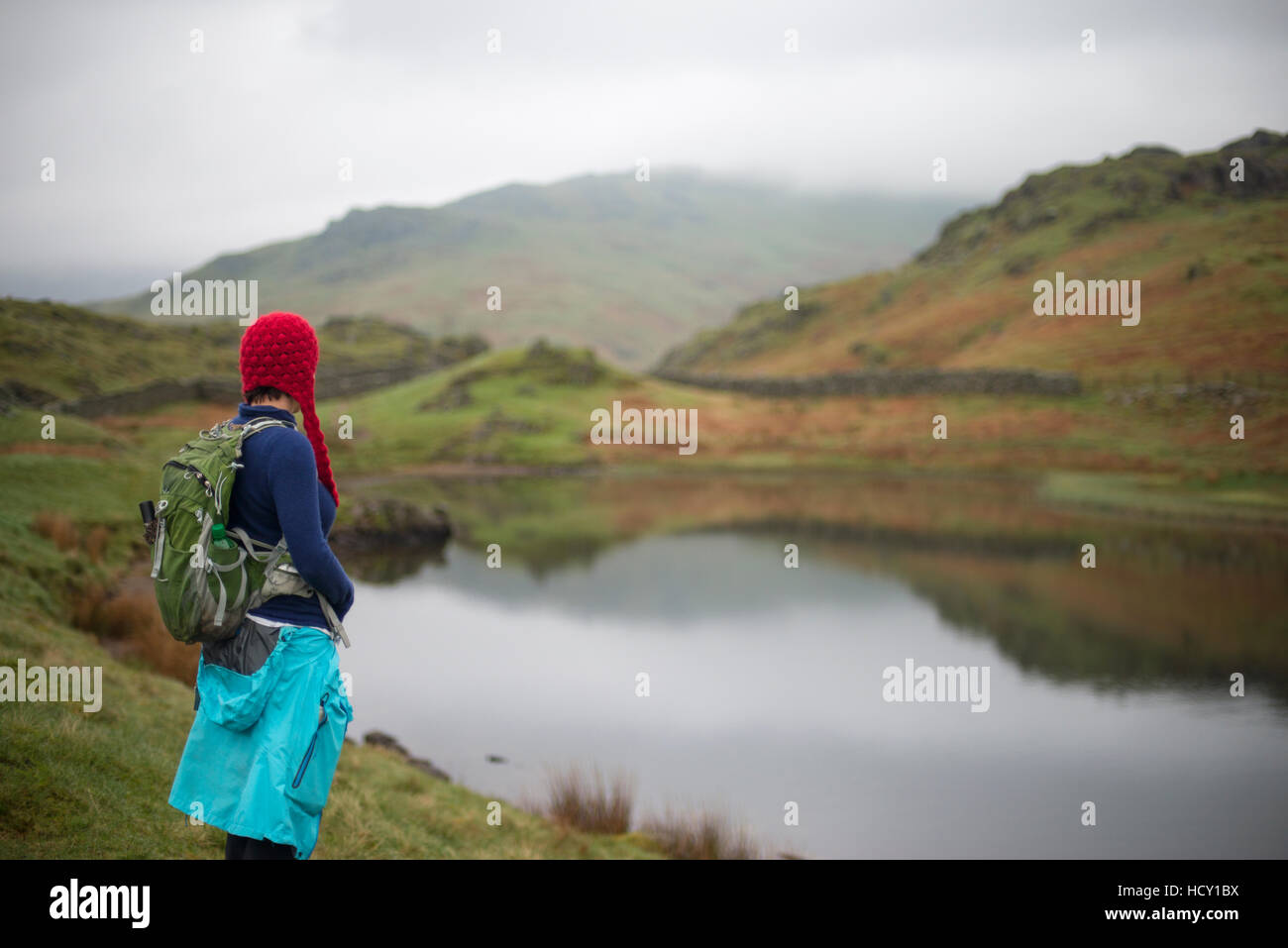 A woman looks out over Alcock Tarn near Grasmere, Lake District, Cumbria, UK Stock Photo