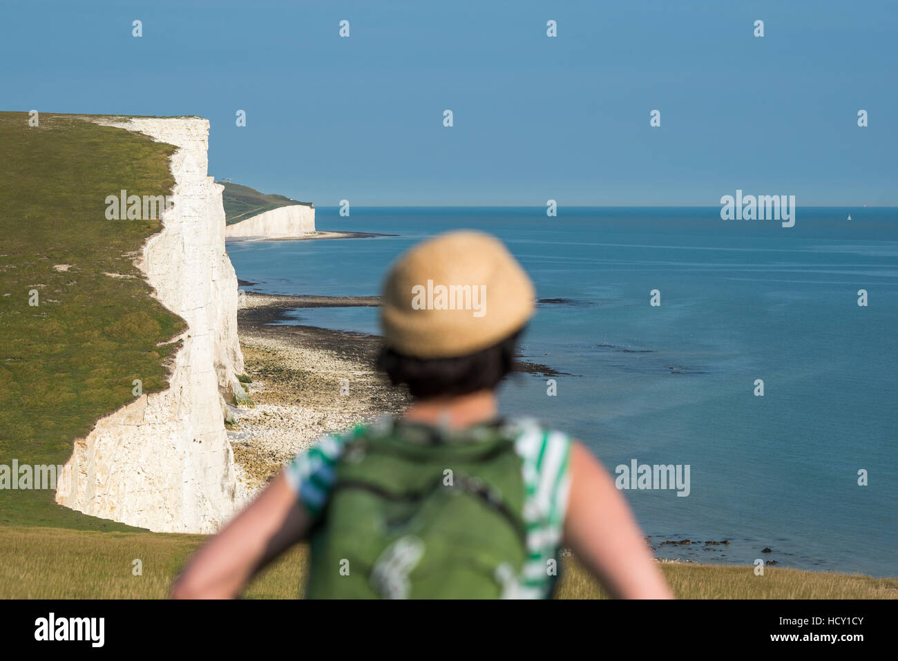 A woman looks out over the cliffs with views of the Seven Sisters coastline, South Downs National Park, East Sussex, UK Stock Photo