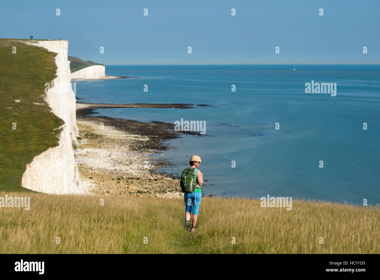 A woman walks along the cliffs near Beachy Head with views of the Seven Sisters coastline, South Downs National Park, UK Stock Photo