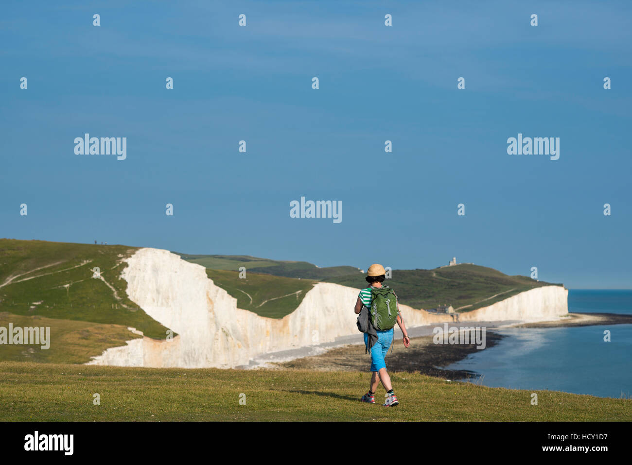 A woman walks along the cliffs near Beachy Head with views of the Seven Sisters, South Downs National Park, East Sussex, UK Stock Photo