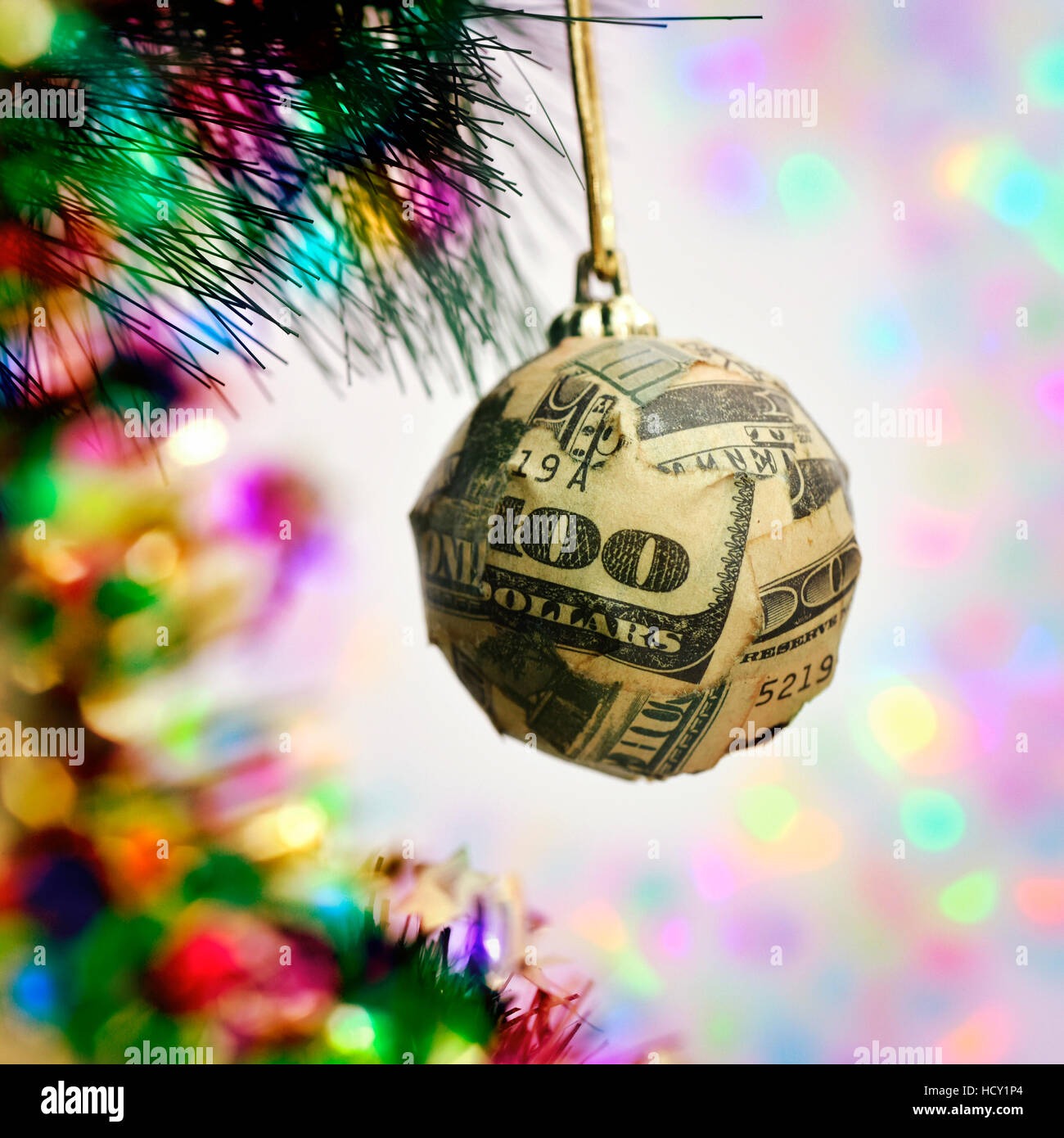 a christmas ball wrapped in pieces of a one hundred dollar banknote hanging from the branch of a christmas tree Stock Photo