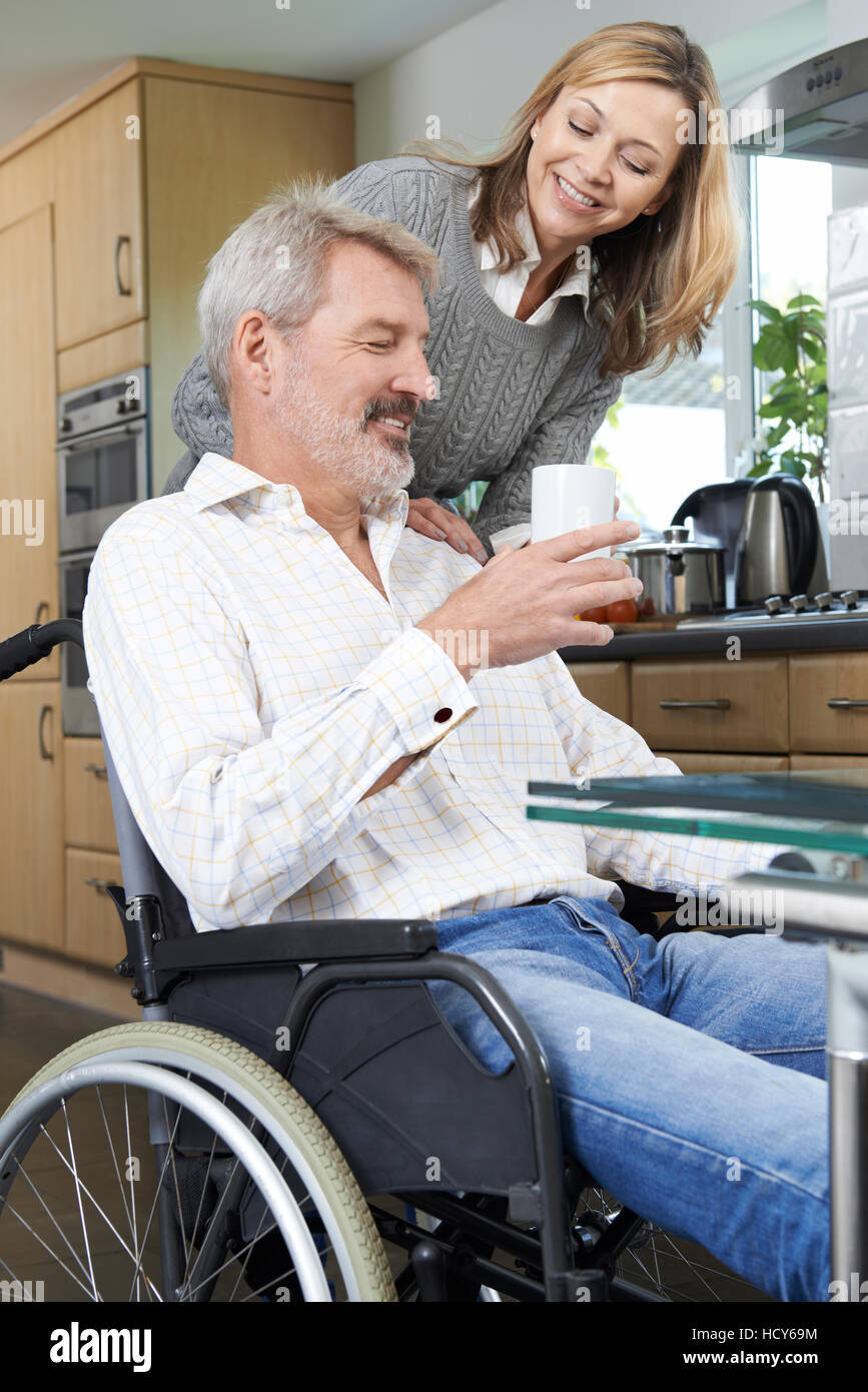 Woman Bringing Man In Wheelchair Hot Drink At Home Stock Photo