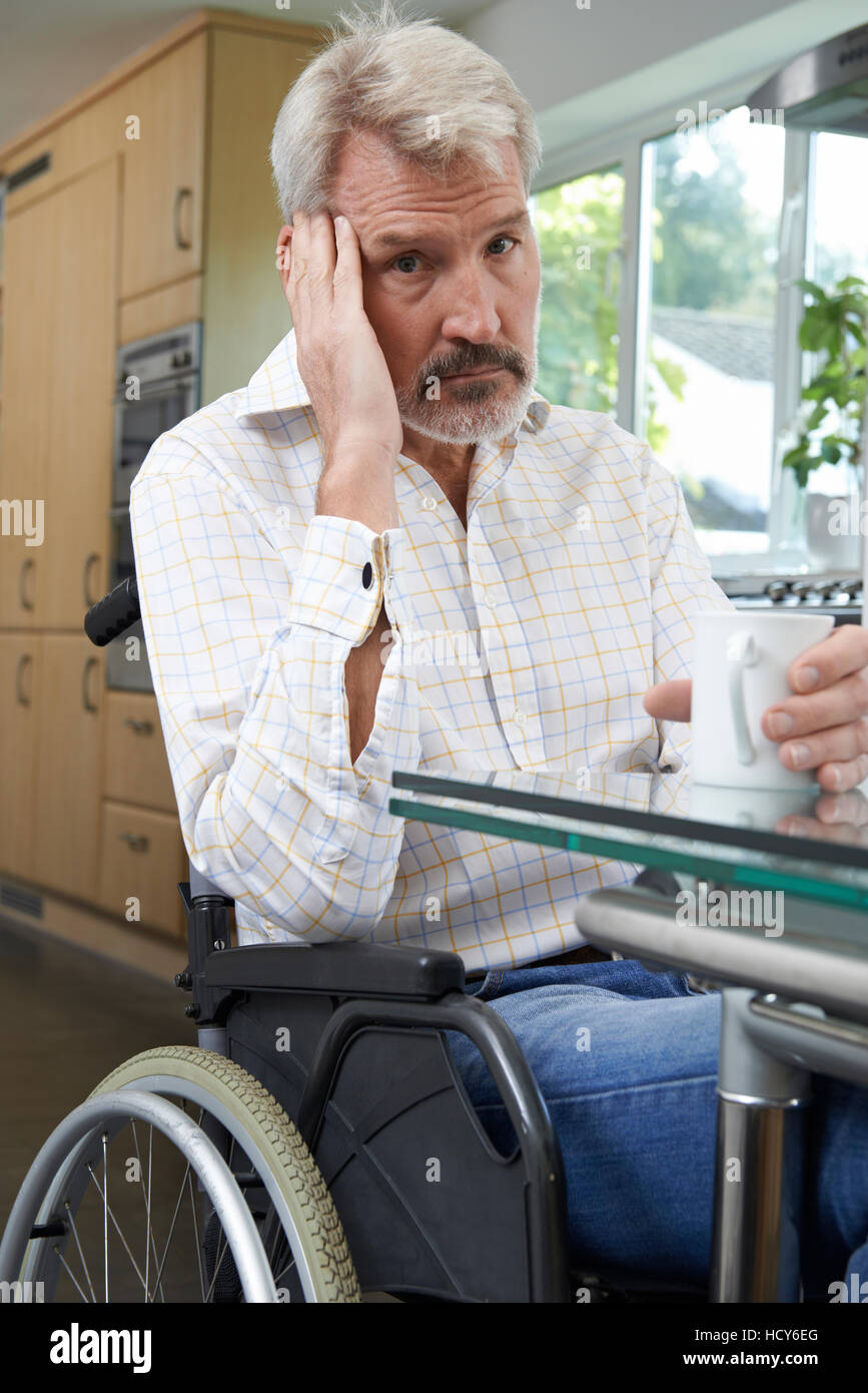 Depressed Man Sitting In Wheelchair At Home Stock Photo