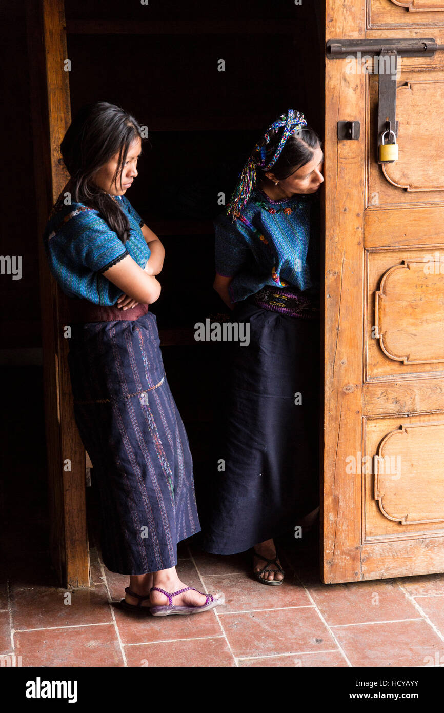 Two Mayan women peering out the door of the Saint Anthony of Padua Church in San Antonio Palopó, Guatemala, wearing typical dress of their village, in Stock Photo