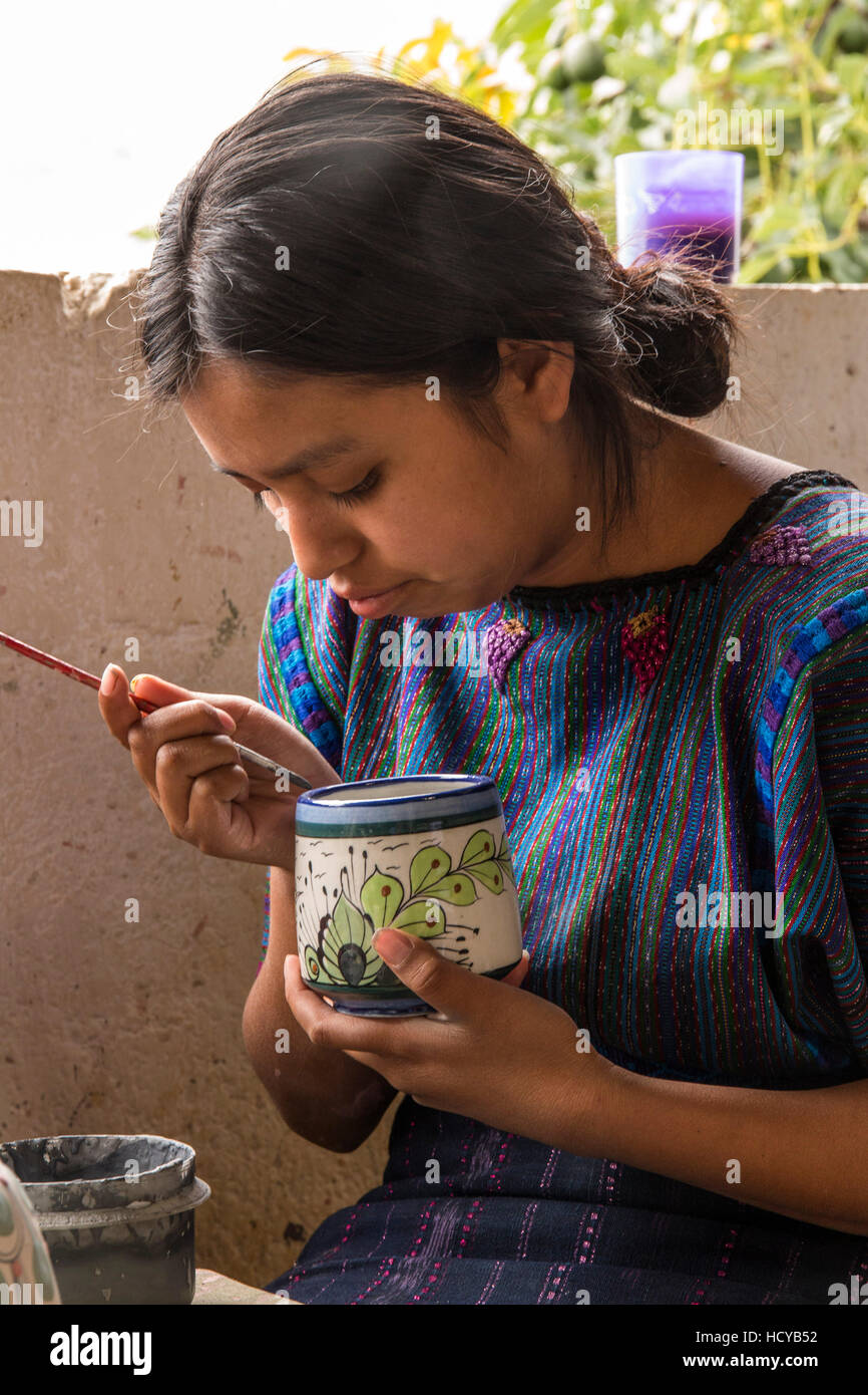 A young Mayan woman, wearing typical traditional dress, paints designs on pottery in a workshop in San Antonio Palopó, Guatemala. Stock Photo