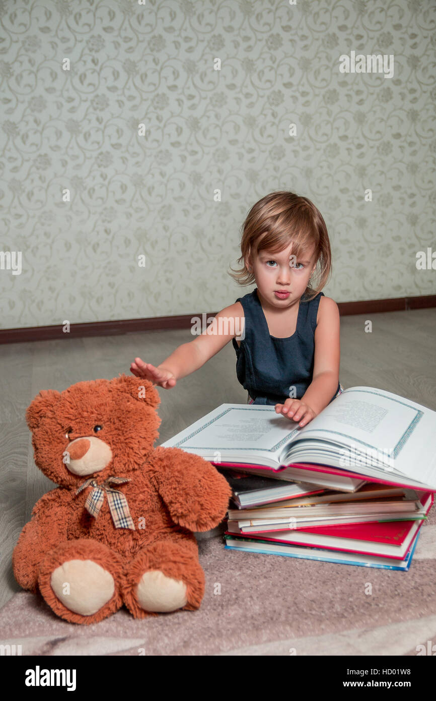 A little girl in a dark blue dress reading a book sitting on the floor ...
