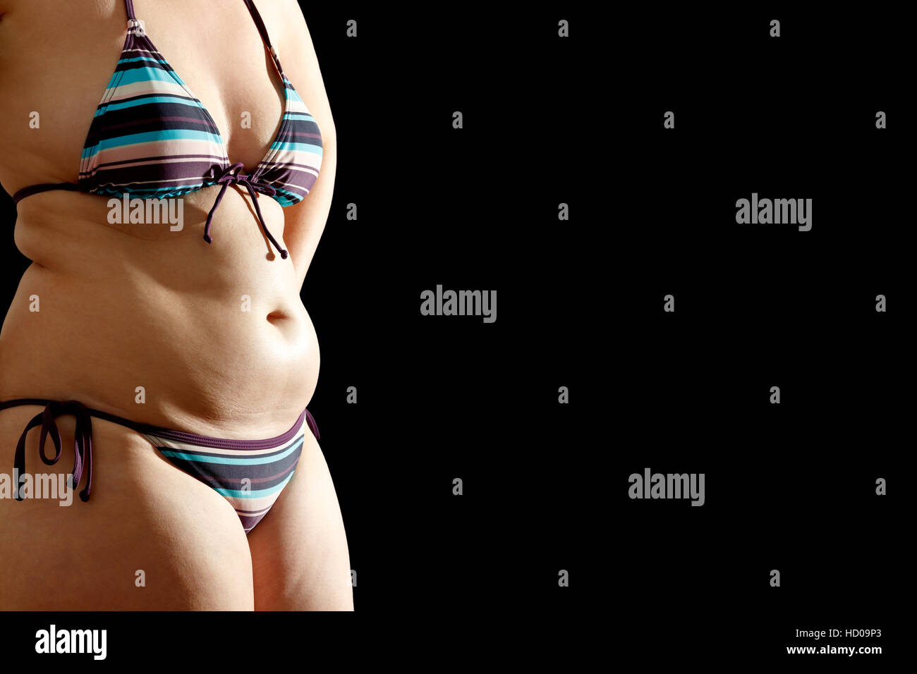 Womans body in bikini with fat rolls on waist and belly on black background, text or copy space Stock Photo