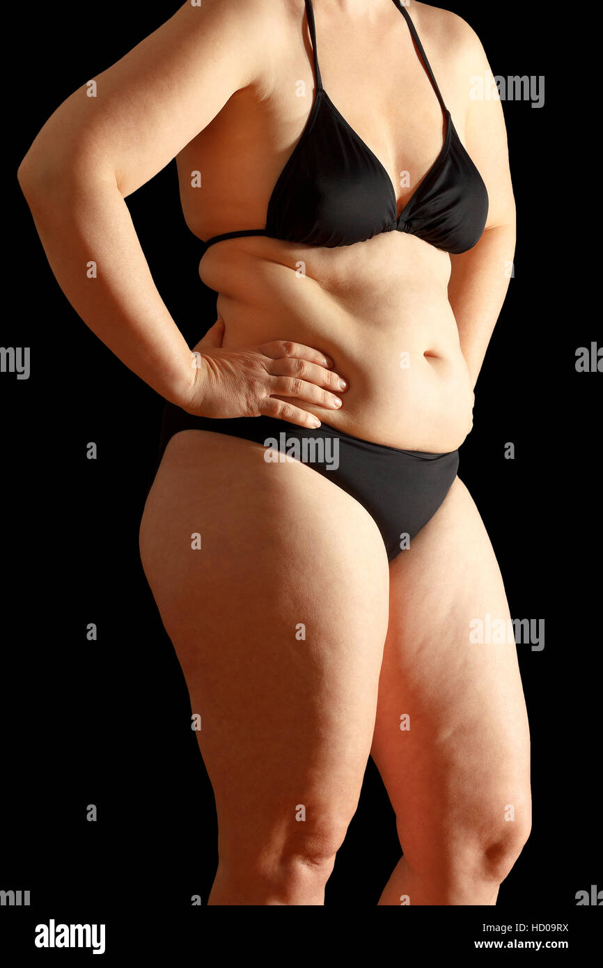 Body of a middle aged woman in bikini with excessive fat on waist and thighs, dimpled skin, black background Stock Photo