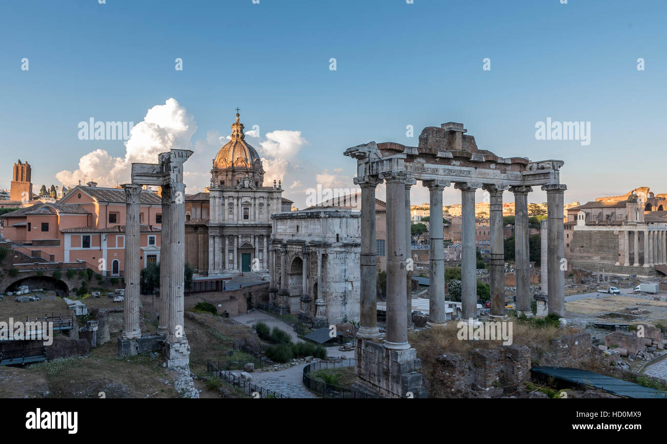 Roman buildings and ruins, in Rome, set against a deep blue sky with large white clouds, tinged with yellow and orange Stock Photo