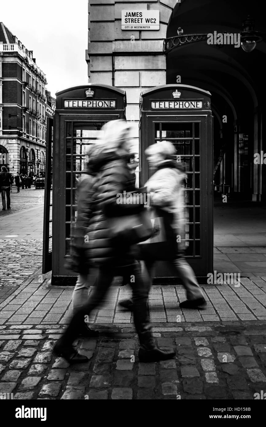 Motion blurred people walking by two telephone booths Stock Photo
