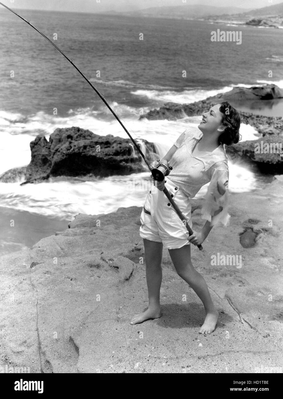 Olivia De Havilland fishing from the shore at Laguna, California, 7/30
