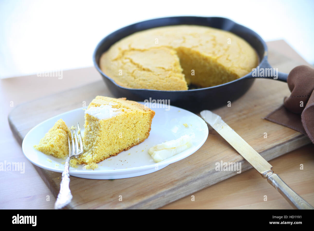Cornbread baked in a cast iron skillet with a wedge on a small dish