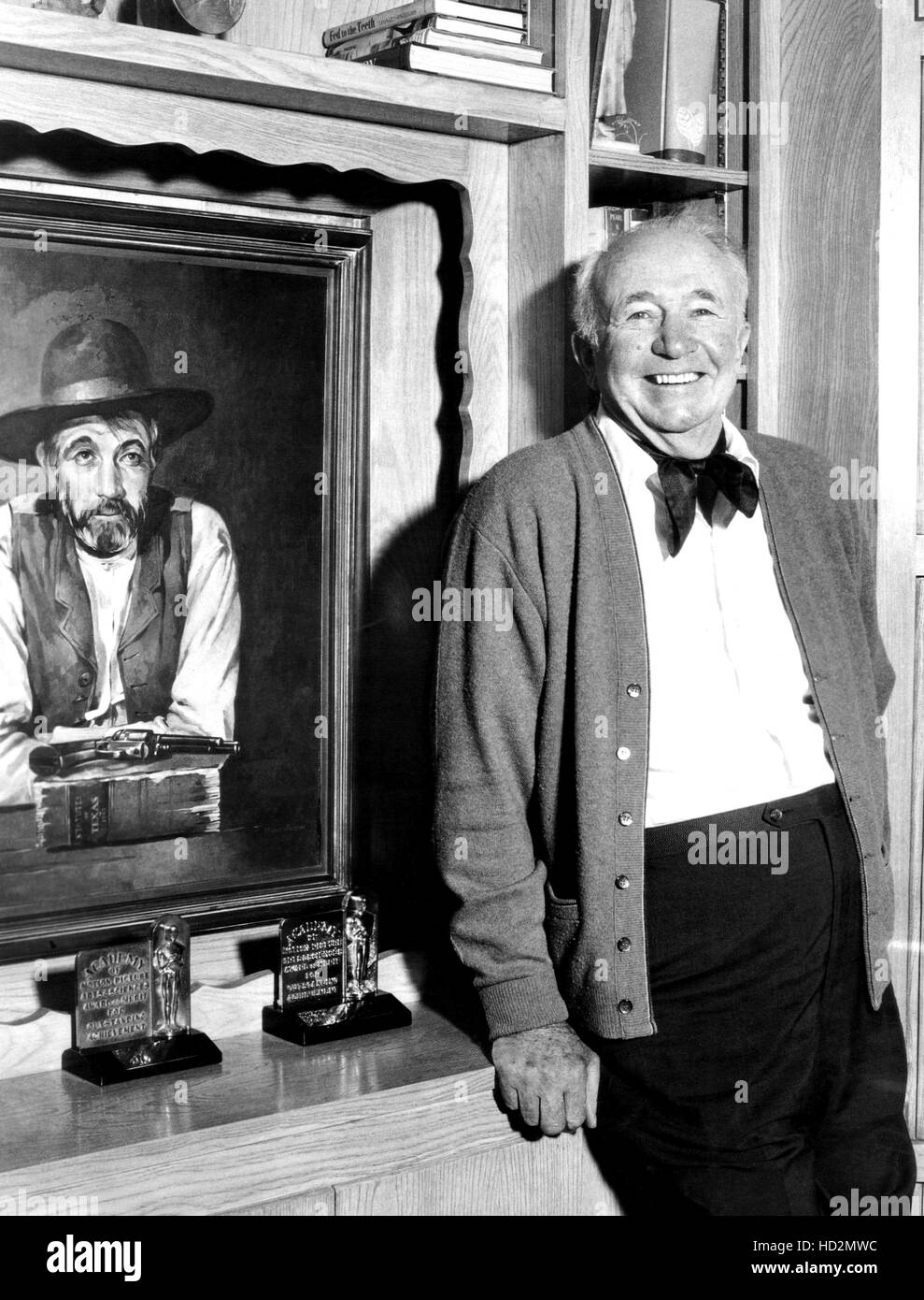 Walter Brennan standing beside a painting of his character in the film