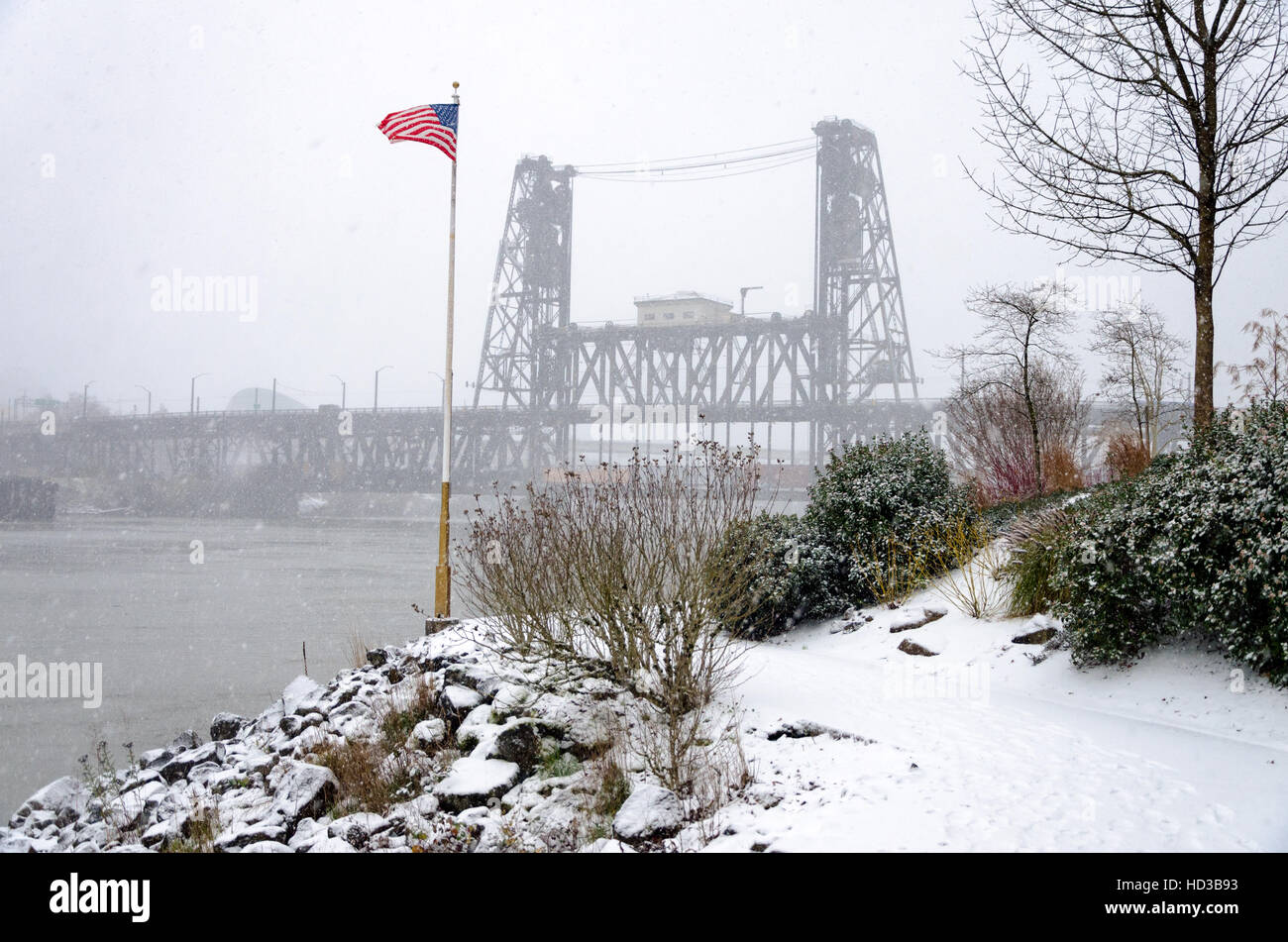 American flag blowing in the wind with the Steel Bridge in the background during a winter snowstorm in Portland, Oregon Stock Photo