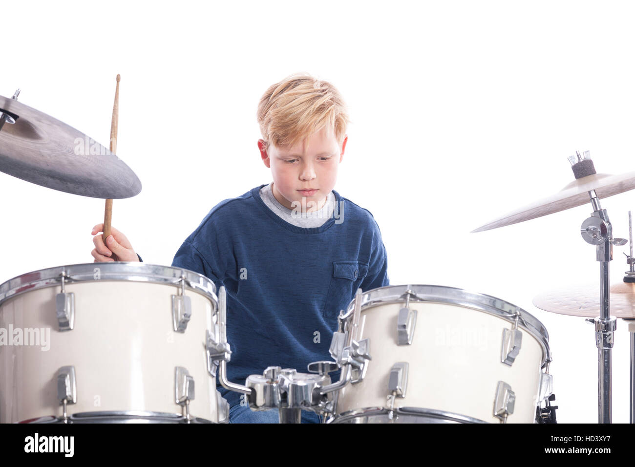 young blond boy drums behind drum kit against white background in studio Stock Photo