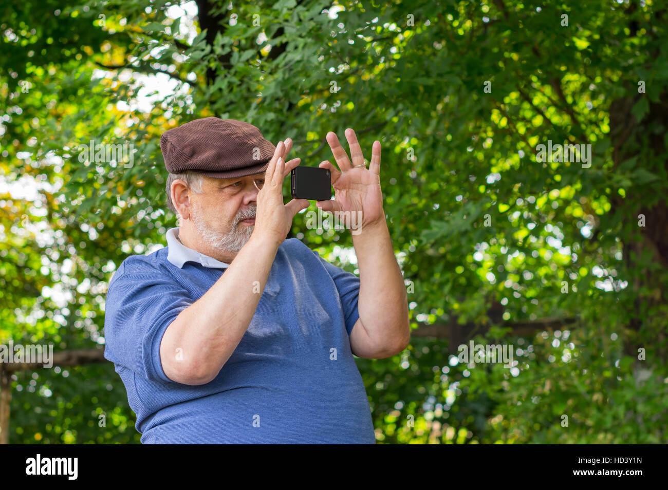 Bearded senior man using cellular phone outdoor making photos with internal camera Stock Photo