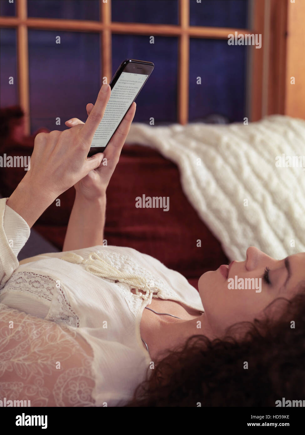 Woman reading book on iPhone 7 Plus at home lying on a sofa Stock Photo