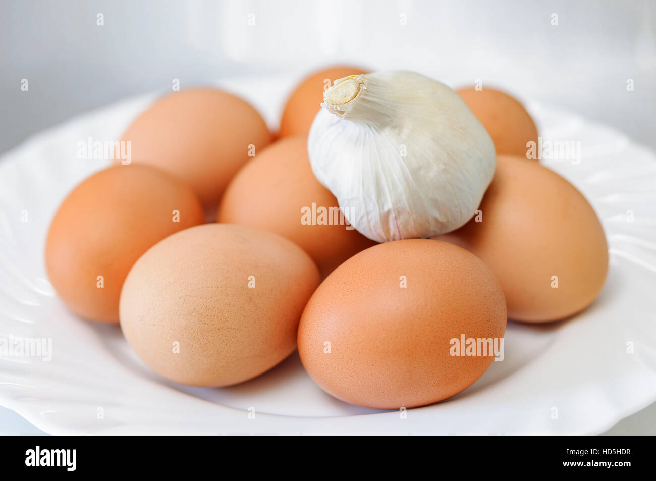 Eight eggs on a white plate of earthenware and a head of garlic on top Stock Photo