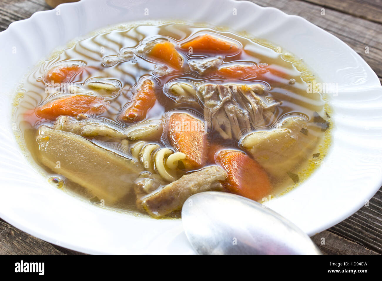 Beef and vegetable broth soup in plate with spoon Stock Photo