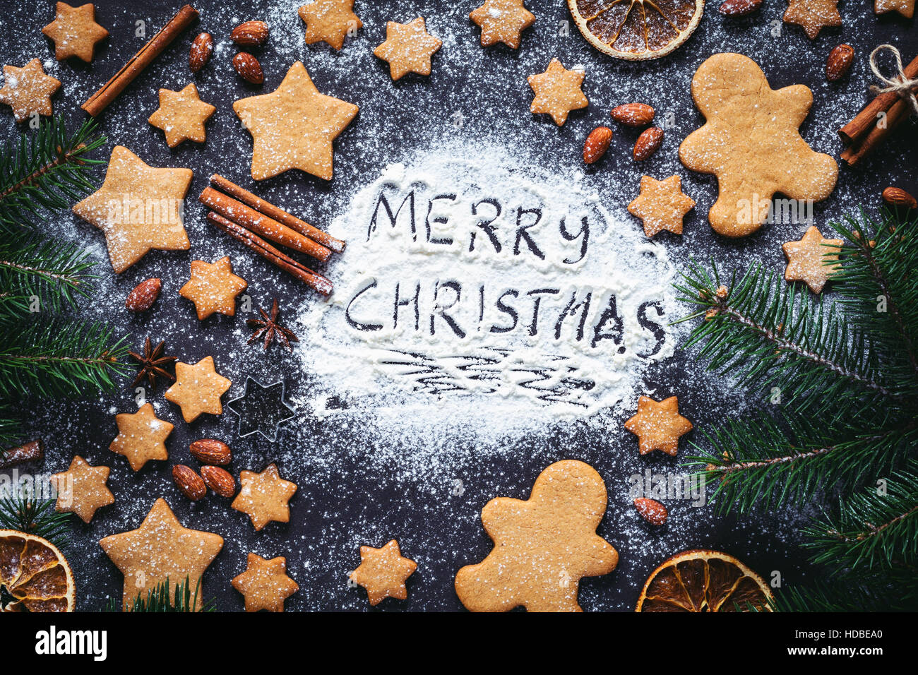 Merry Christmas greeting written on flour on blackboard. Frame with gingerbread cookies, gingerbread man cookies and spices Stock Photo