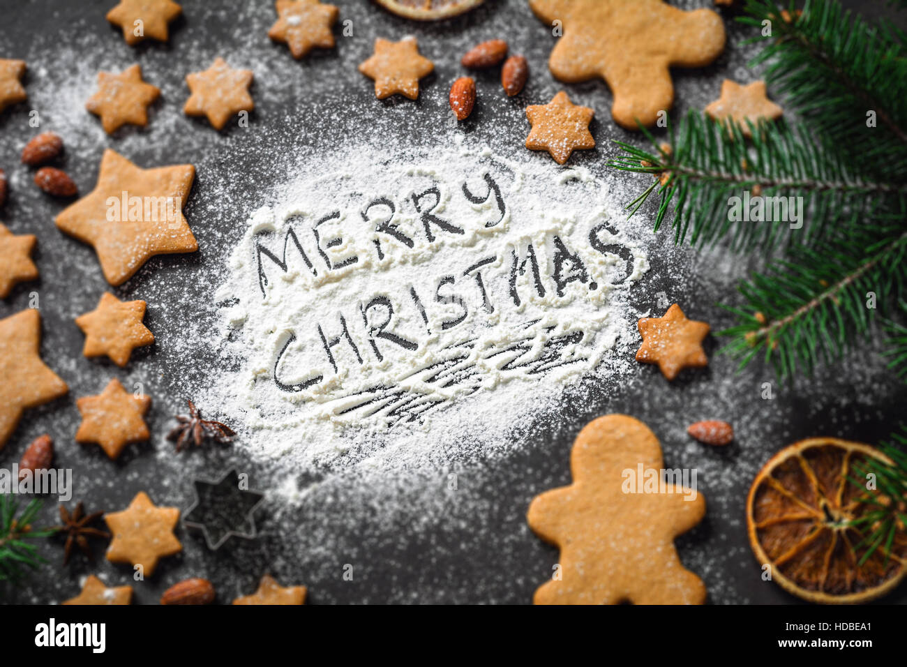 Merry Christmas greeting written on flour. Christmas holidays card with gingerbread cookies, spices, fir tree. Selective focus Stock Photo