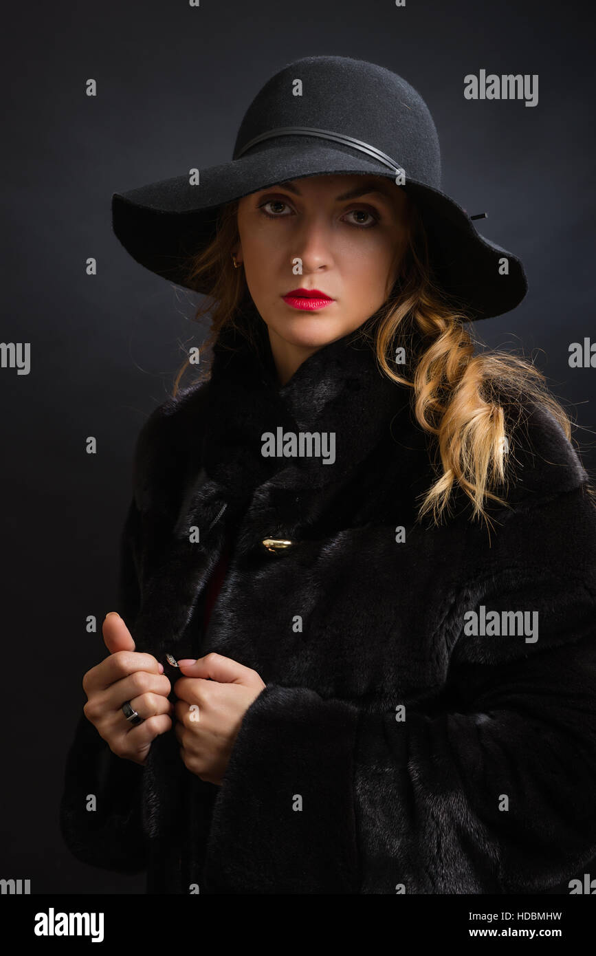 The beautiful young girl in a black hat with wide fields and fur coat