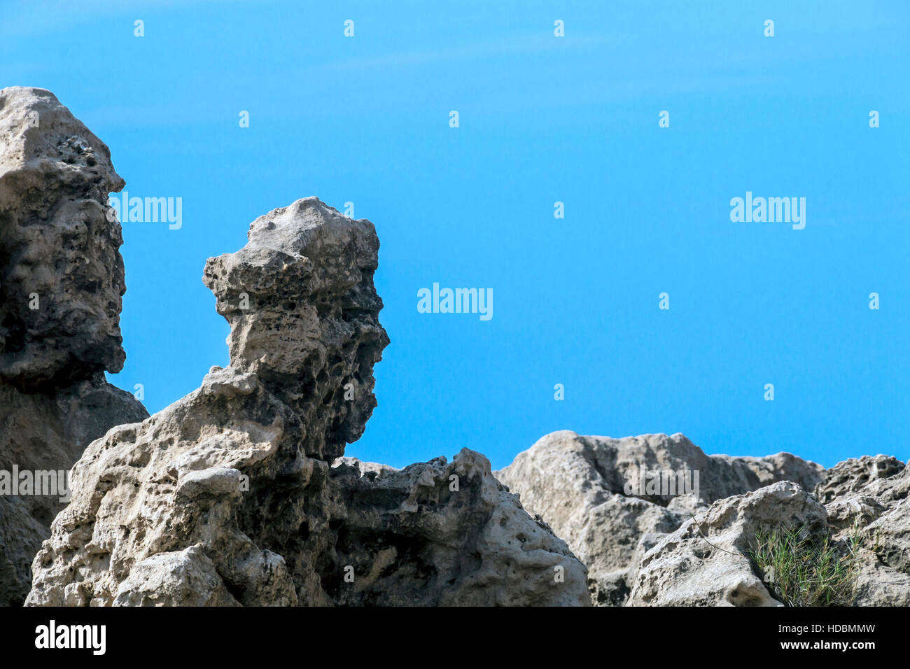 Rocks weathered into strange human-like formations on beach against blue sky Stock Photo