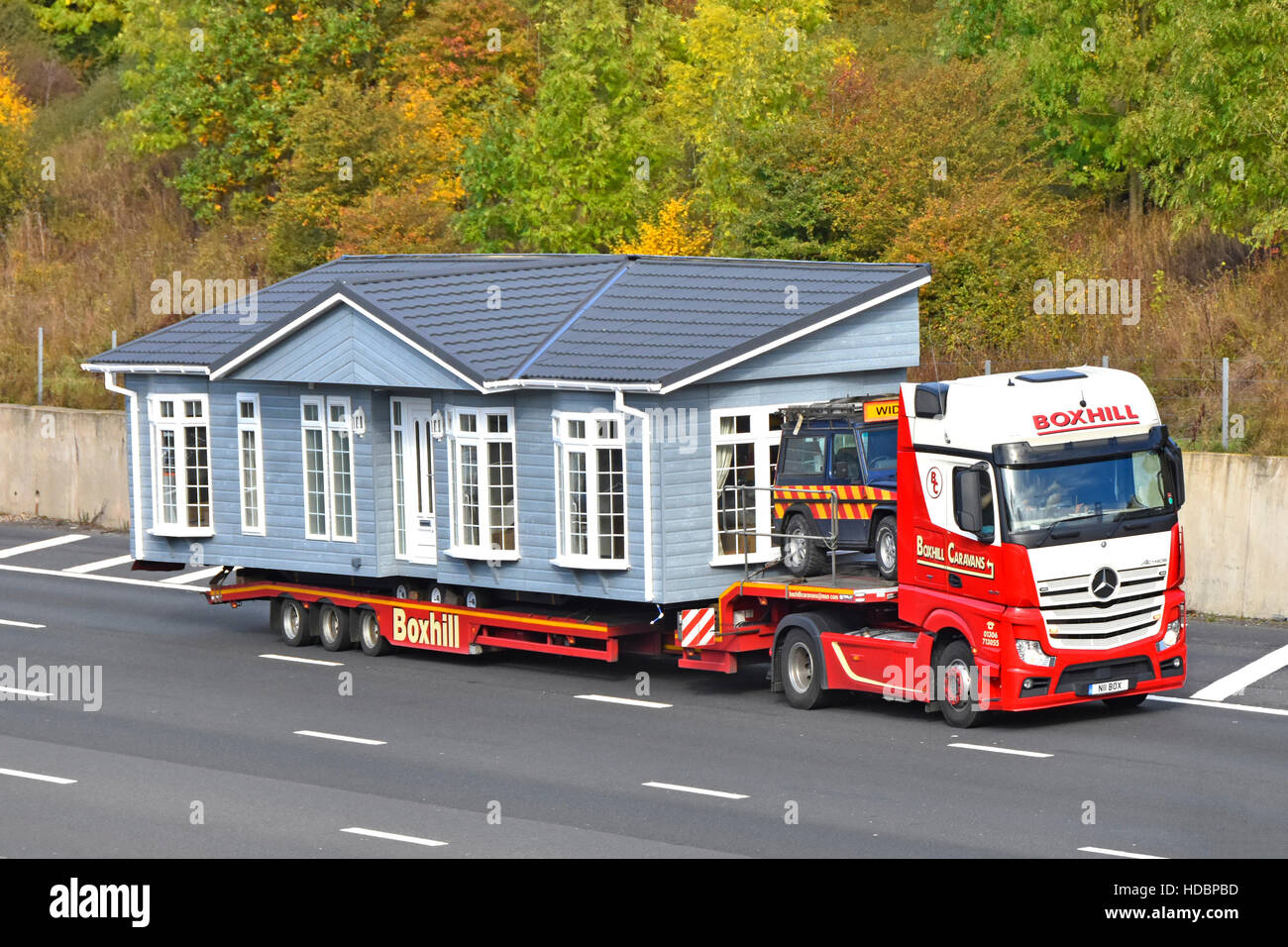 Park Home lodge part of oversize factory assembled prefabricated wide load transported on UK motorway hgv low loader articulated truck with escort car Stock Photo