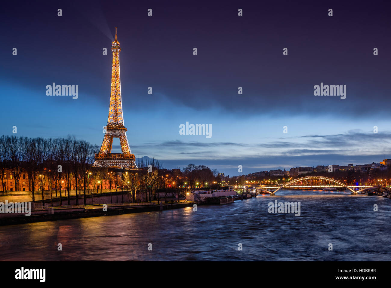 The Eiffel Tower illuminated at twilight with banks of the Seine River and the Debilly Footbridge. Paris, France Stock Photo