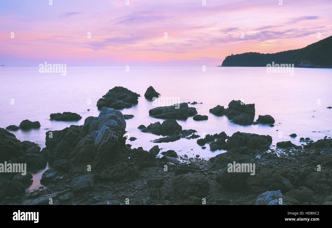 Black rock beach with smooth milky sea surface and pink twilight sky ...