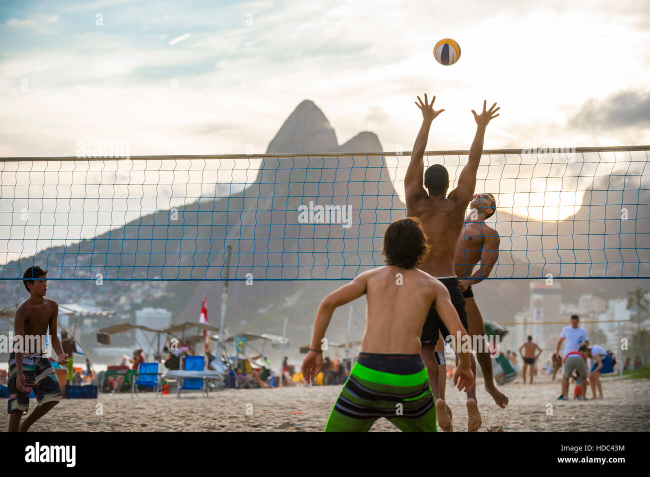 RIO DE JANEIRO - MARCH 20, 2016: Young carioca Brazilians play beach volleyball against a sunset silhouette of Ipanema Beach. Stock Photo