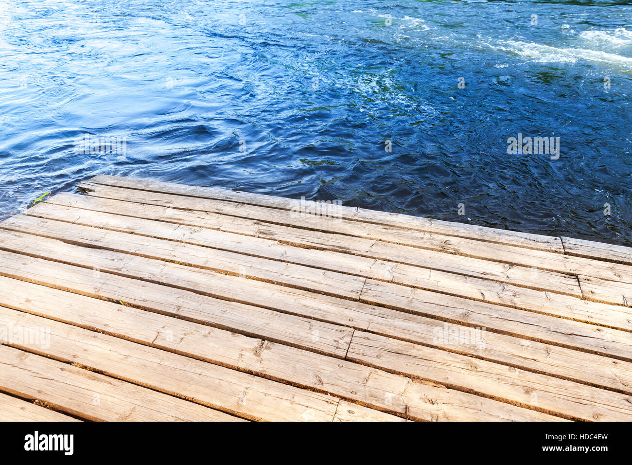 Corner of an old wooden pier with blue river water on a background Stock Photo