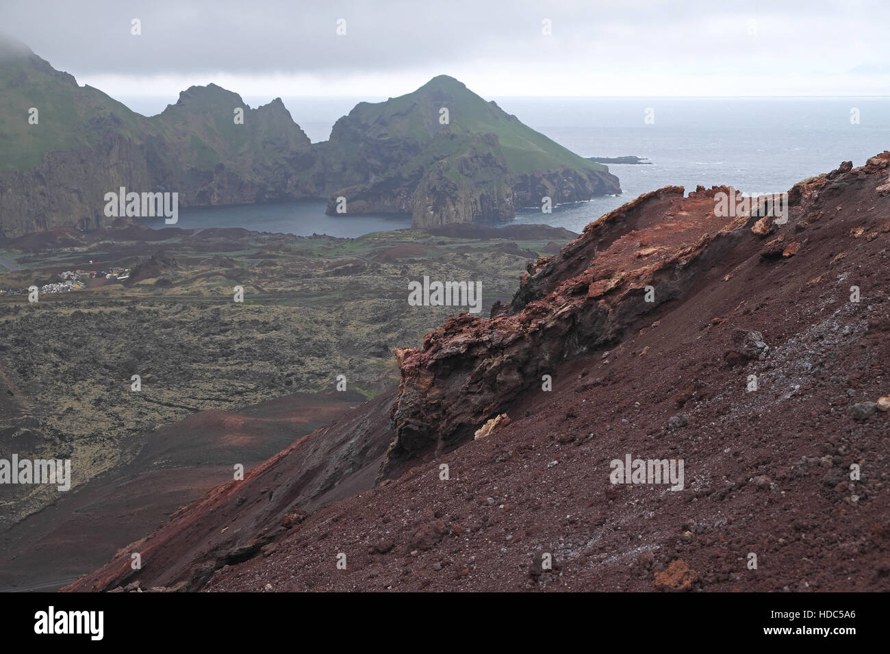 Part of Heimaey (left) seen over volcanic rocks and lava field from flanks of Eldfell, Heimaey, Vestmannaeyjar Islands, Iceland. Stock Photo