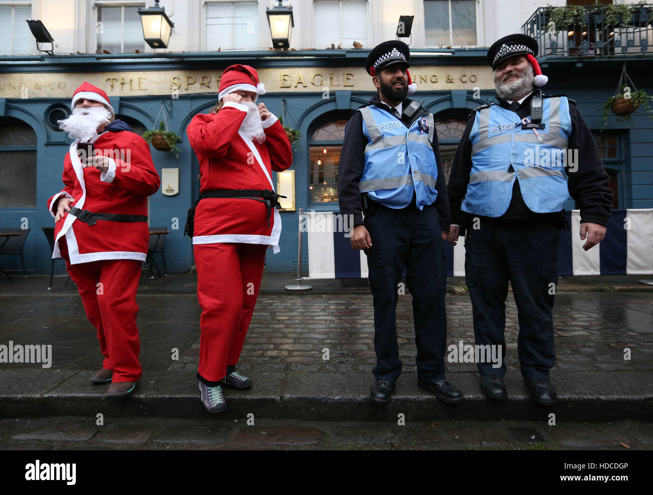 Police officers wearing santa hats underneath their caps, outside the Spread Eagle pub on Albert Street in Camden, north London, as hundreds of revellers take part in the Santacon Christmas parade. Stock Photo
