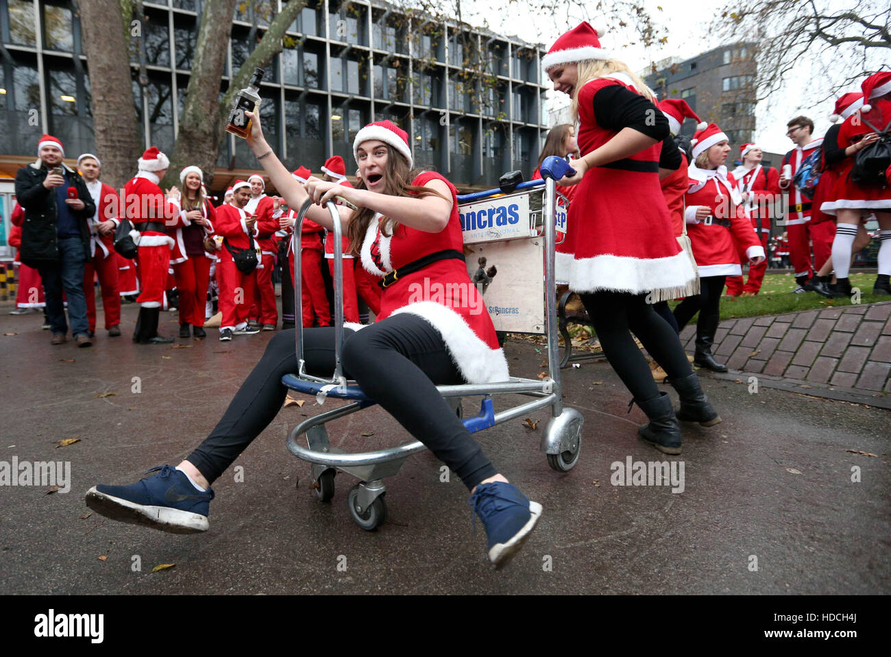 Revellers dressed in Santa suits push each other round on a luggage