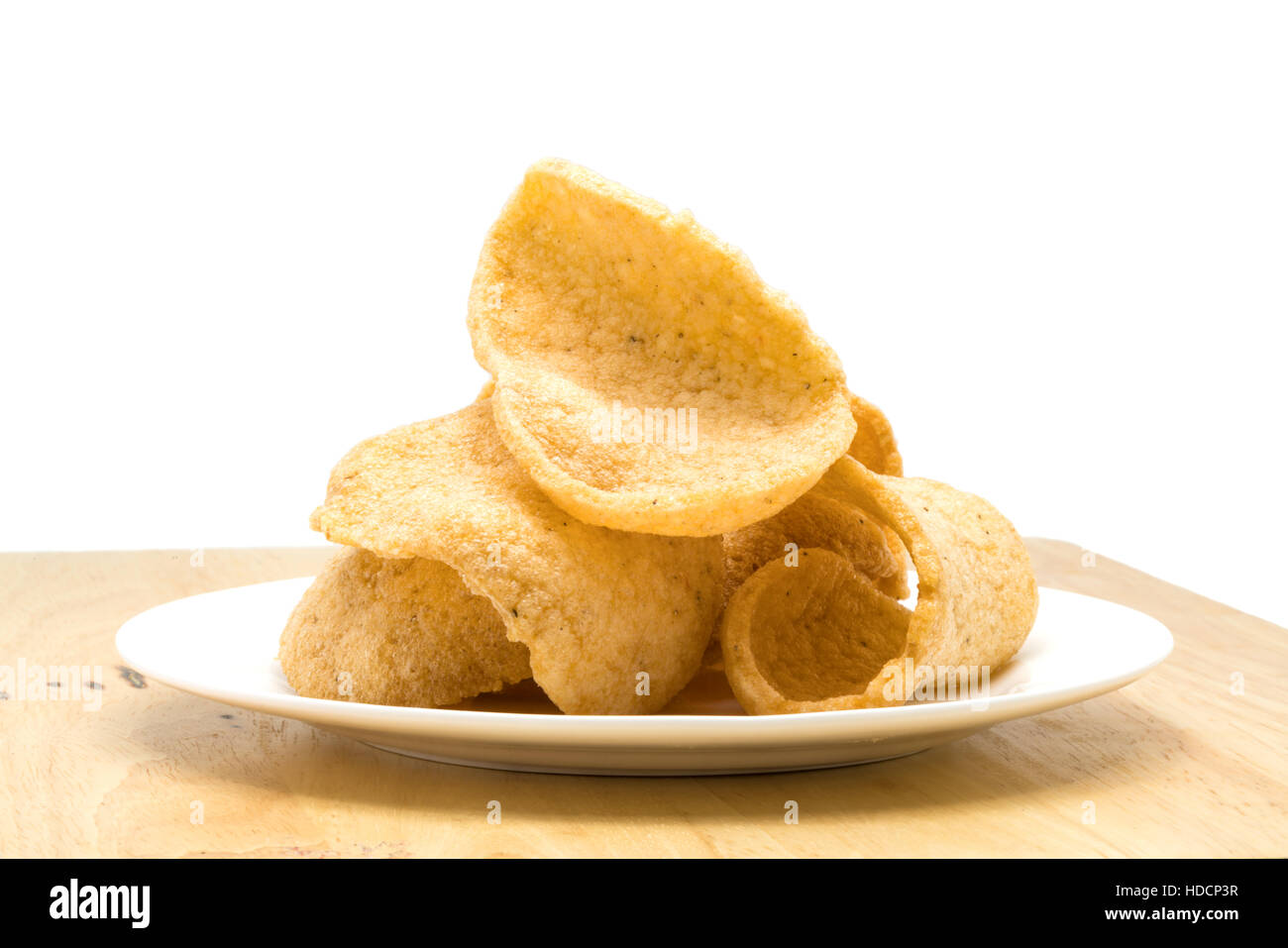 Pile of crunchy prawn cracker in a white plate on a wooden board on white background Stock Photo