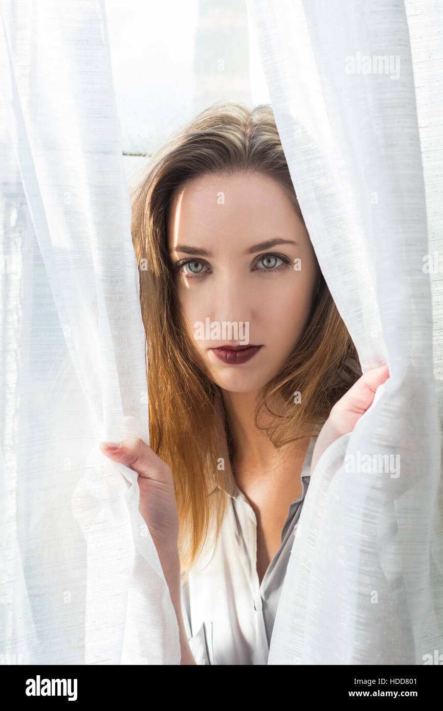 Beautiful young woman looking through the blinds Stock Photo