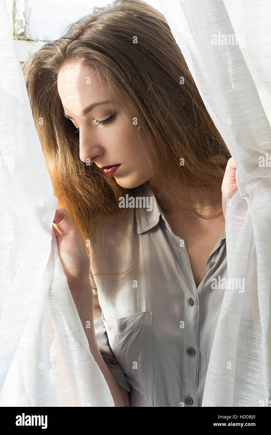 Sad woman holding the blinds looking down Stock Photo