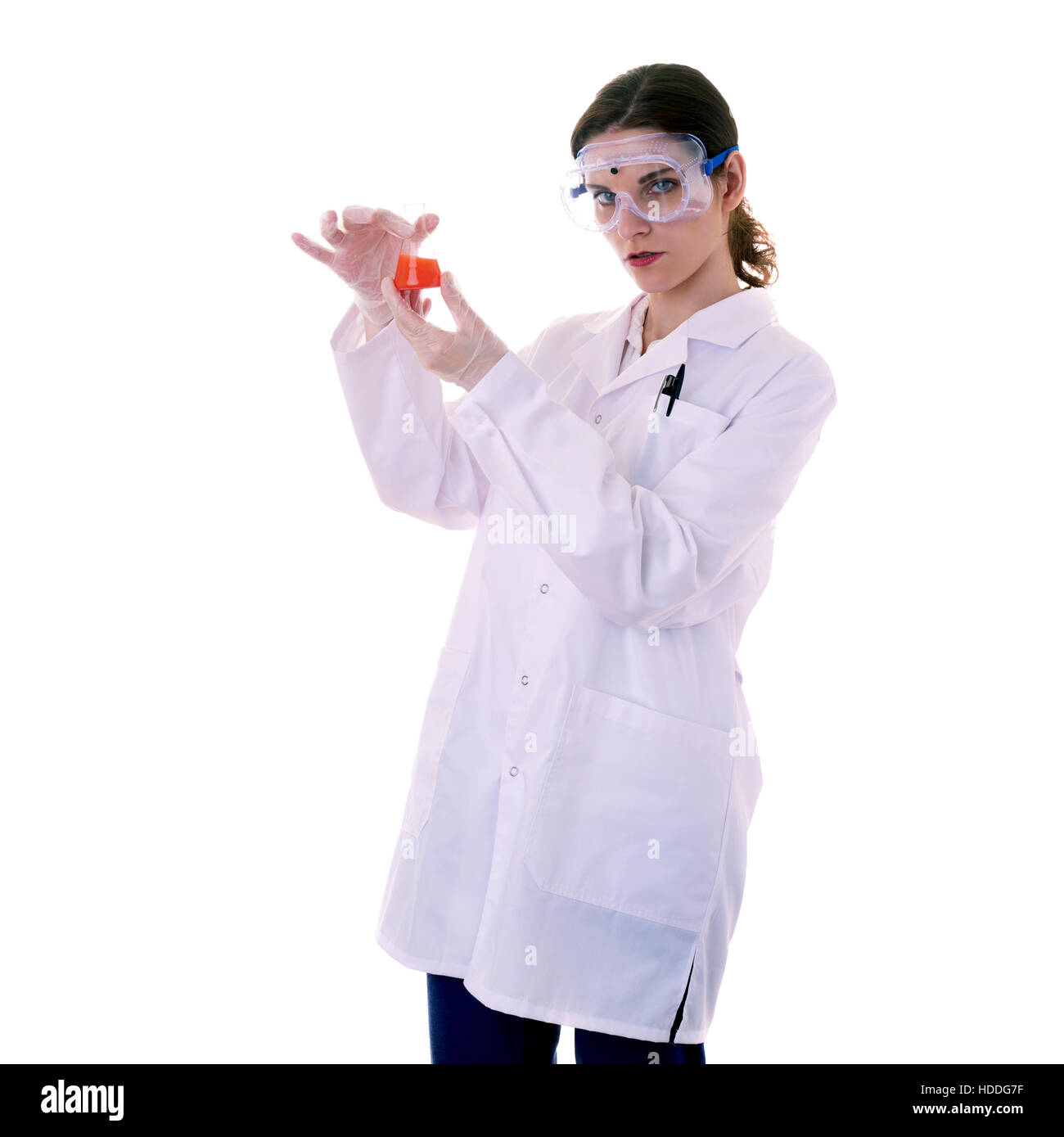Female assistant scientist in white coat and plastic protective glasses over white isolated background inspecting flask filled with substance, healthc Stock Photo