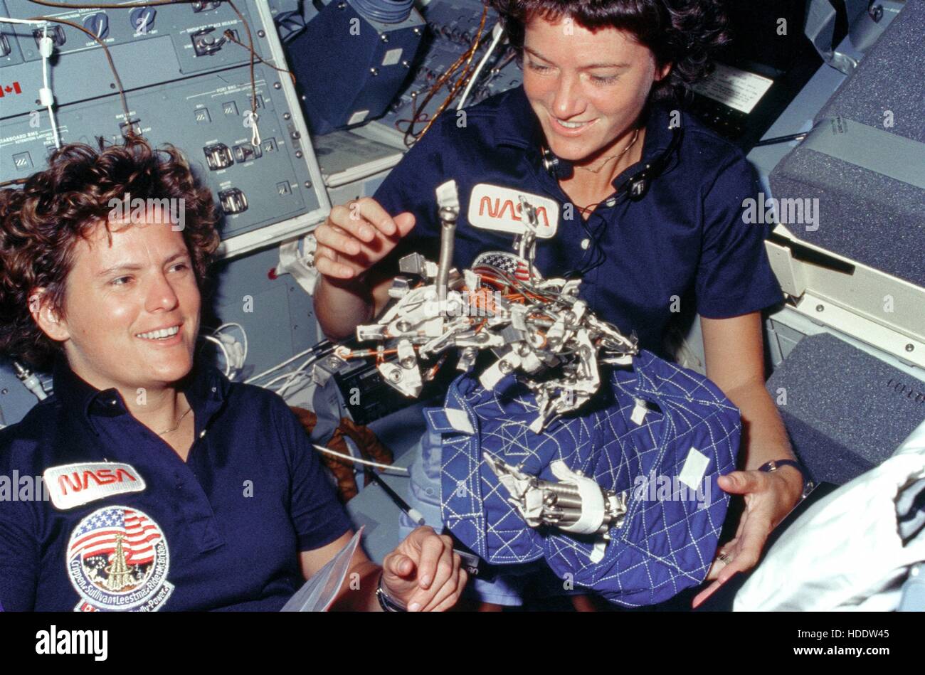 NASA STS-41G mission crew members astronauts Kathryn Sullivan (left) and Sally Ride show off their “bag of worms” sleep restraint system invention October 6, 1984 aboard the Space Shuttle Challenger in Earth orbit. The “bag” is a sleeping restraint and the “worms” consist of springs, clips, clamps, bungee cords, and Velcro strips to aid in restraint. Stock Photo