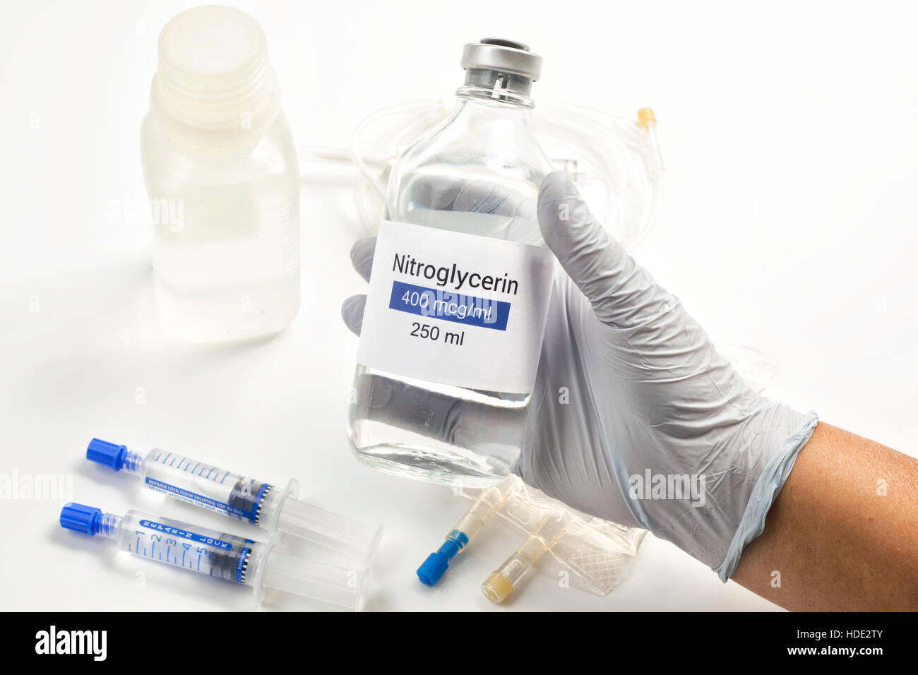 Nitroglycerin IV bottle held by nurse with heparin lock syringes. Stock Photo