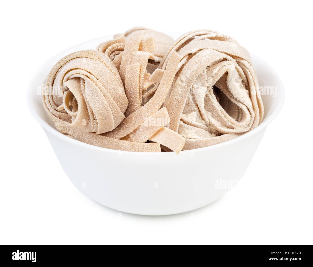 Dry homemade rolled traditional italian pasta  in bowl isolated on white background. Raw fettuccine or tagliatelle or pappardelle. Stock Photo