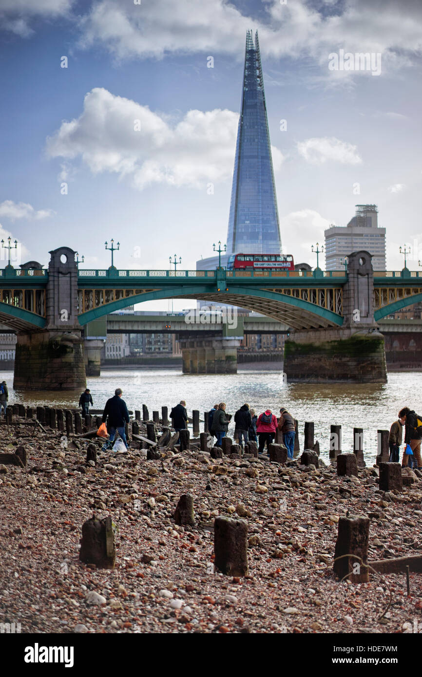 Low tide on the Thames bank below Southwark Bridge in London where visitors hunt for items washed up, in front of the Shard. Stock Photo