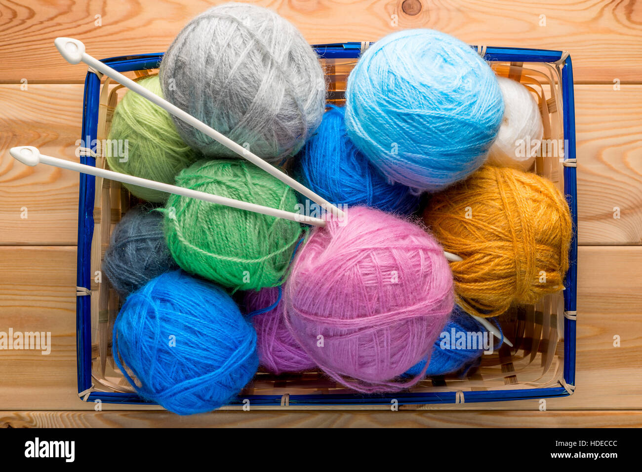 basket stuffed with balls of yarn and knitting needles on wooden boards ...