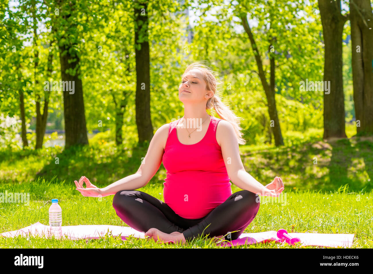 happy pregnant woman in a lotus position doing yoga in the park Stock Photo